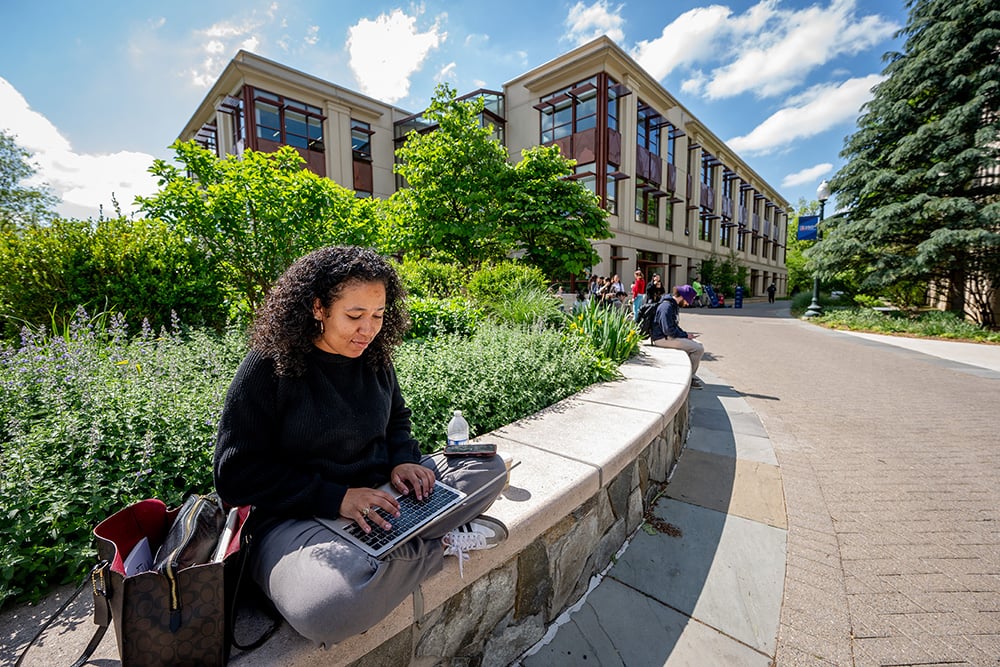 A student works on a laptop outside the SIS building on a sunny day.
