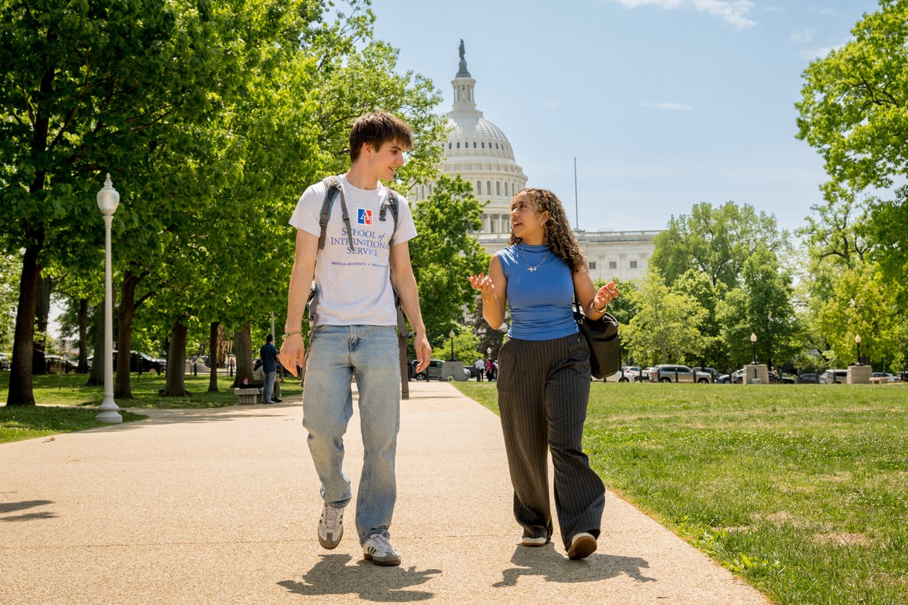 Two SIS students talk and walk on a sunny day with the U.S. Capitol behind them.