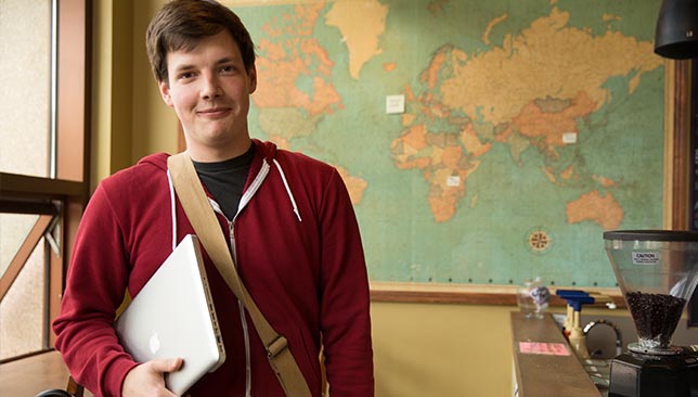 students stands with laptop in front of world map