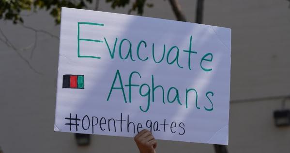 A sign is held up, which says "Evacuate Afghans #openthegates."