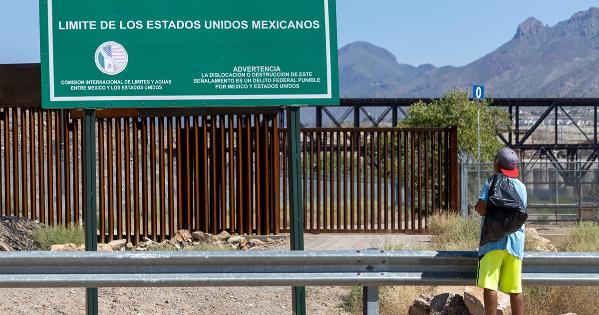 Migrant walks on road in front of sign for US border in Spanish