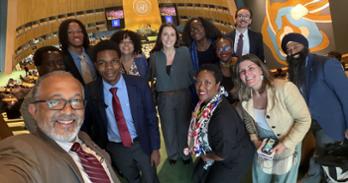 A group of students smile for a photo with Professor Derrick Cogburn
