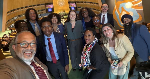 A group of students smile for a photo with Professor Derrick Cogburn