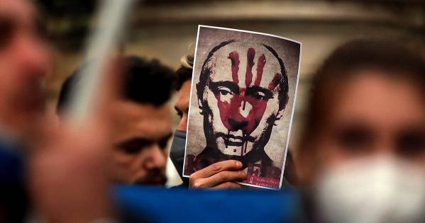 Protesters of war in Ukraine, one holdiing image of Vladimir Putin with bloody handprint over his face.