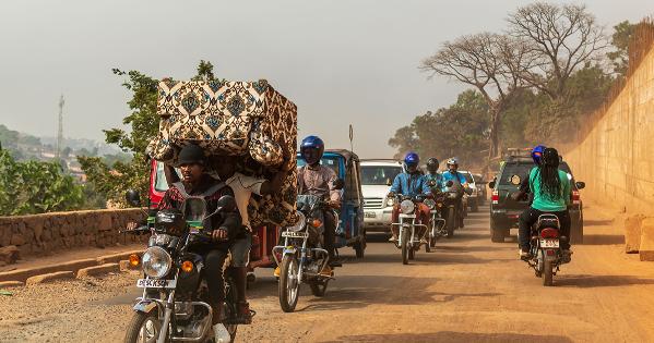 A group of men on motorcycles rides down a dirt road in Sierra Leone