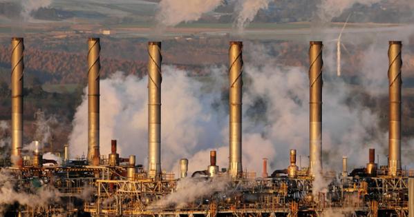 Several oil refinery chimneys expelling smoke in a mountainous area.