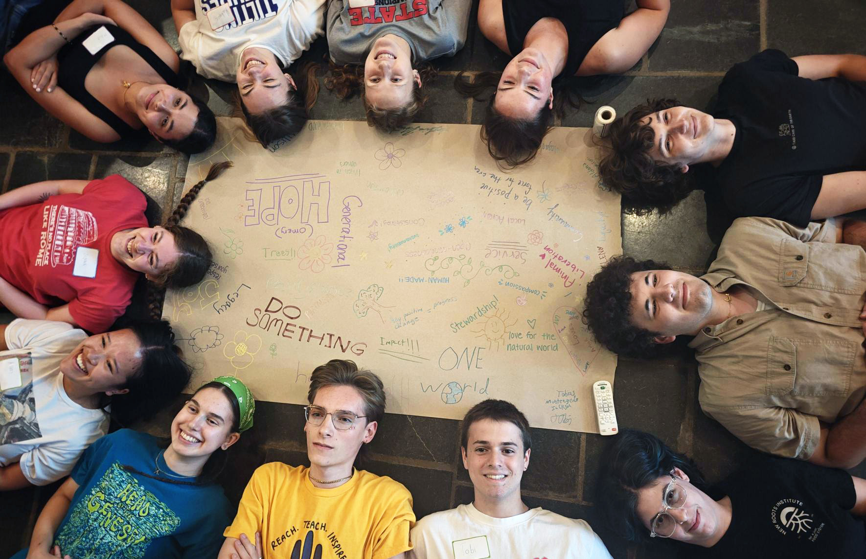 Smiling Earth Scholars lie in a circle around handwritten messages on a poster looking up at the camera.
