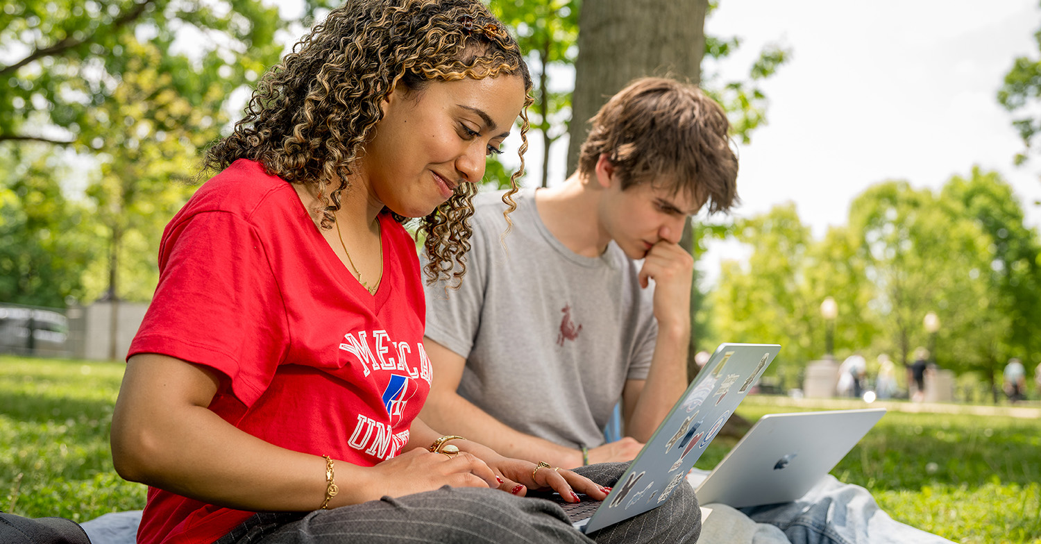 Two SIS students work on their laptops in front of the U.S. Capitol.