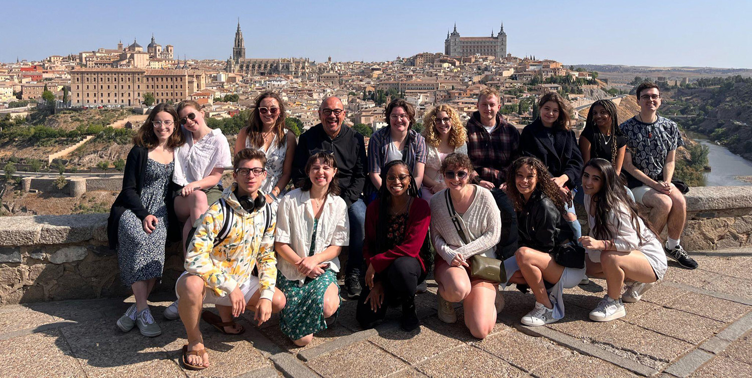 A groupf students, faculty, and staff pose for a photo with the Toledo, Spain, skyline behind them.