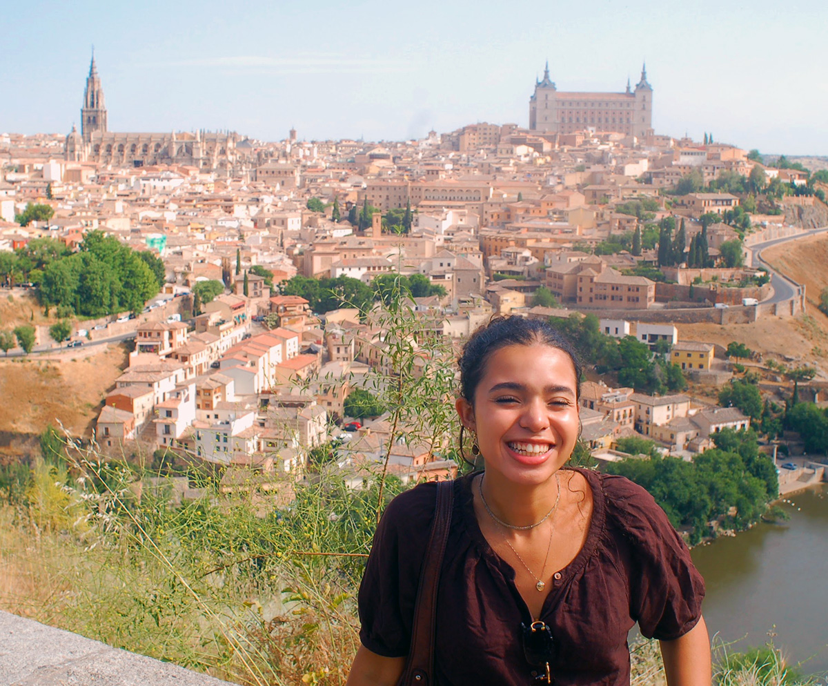 A young woman stands in front of a sprawling view of Toledo, Spain.