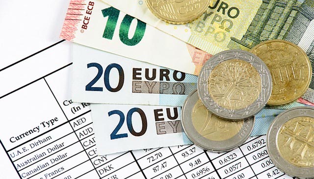foreign currency laid out on a table on top of a spreadsheet of exchange rates