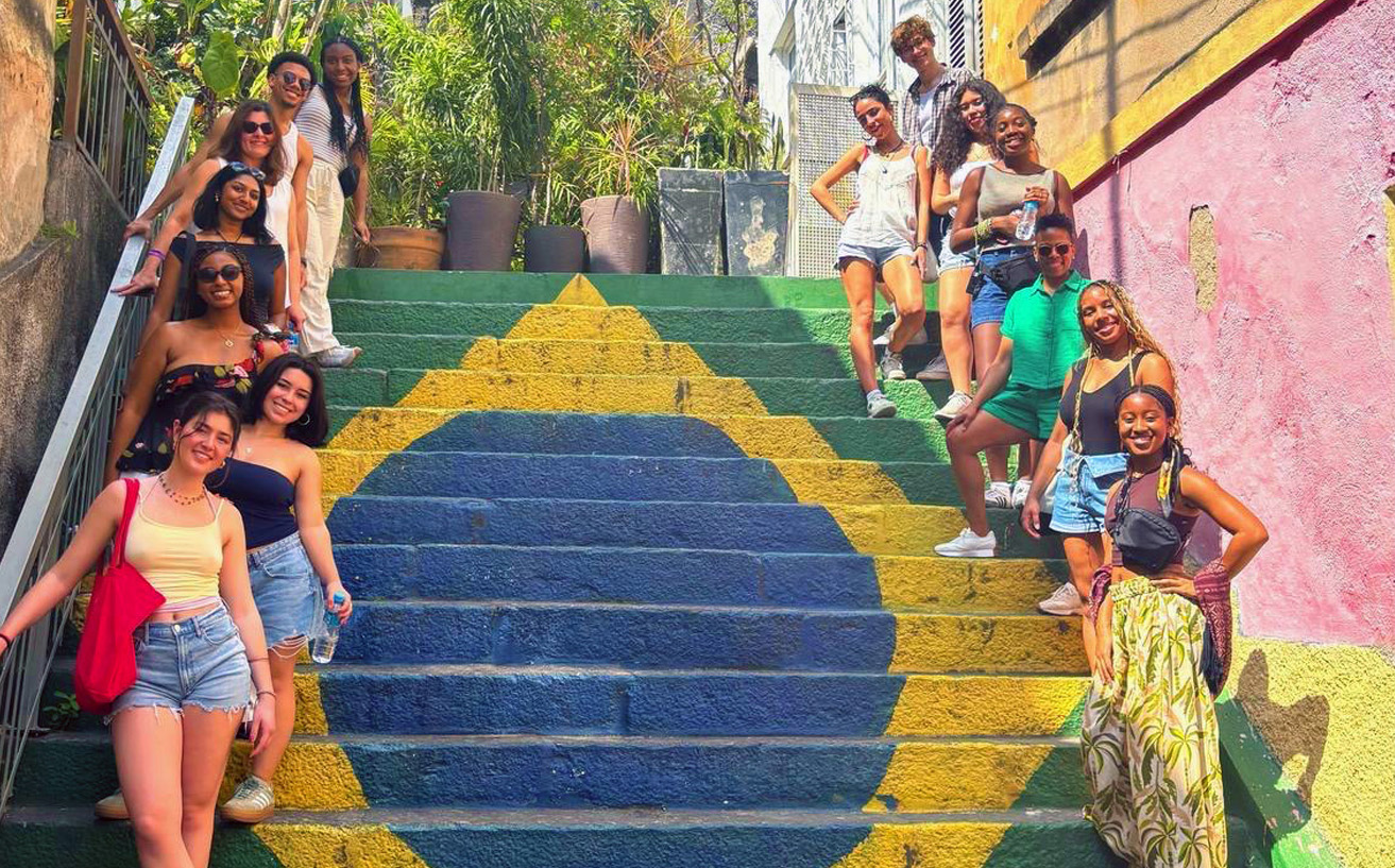 Students abroad in Brazil posing and smiling on steps with the Brazil flag.