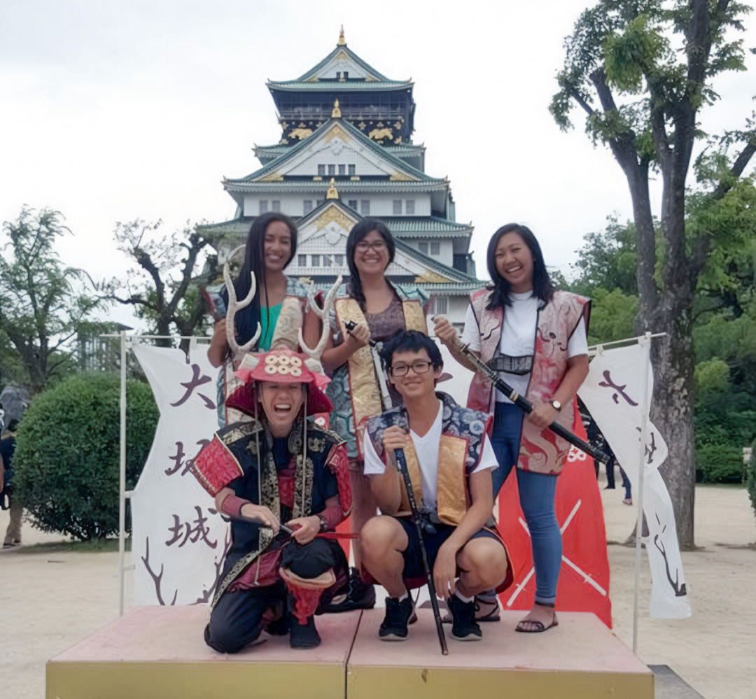 A group of smiling students wear traditional samurai armor and hold katanas in Japan.