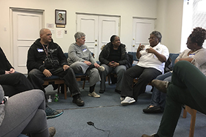 A group of people sitting in a circle of chairs talking