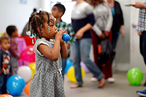 A little girl blowing up a balloon