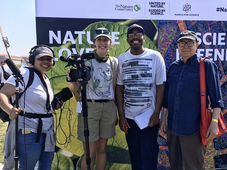 Three students and a professor pose with film gear at the march for science.