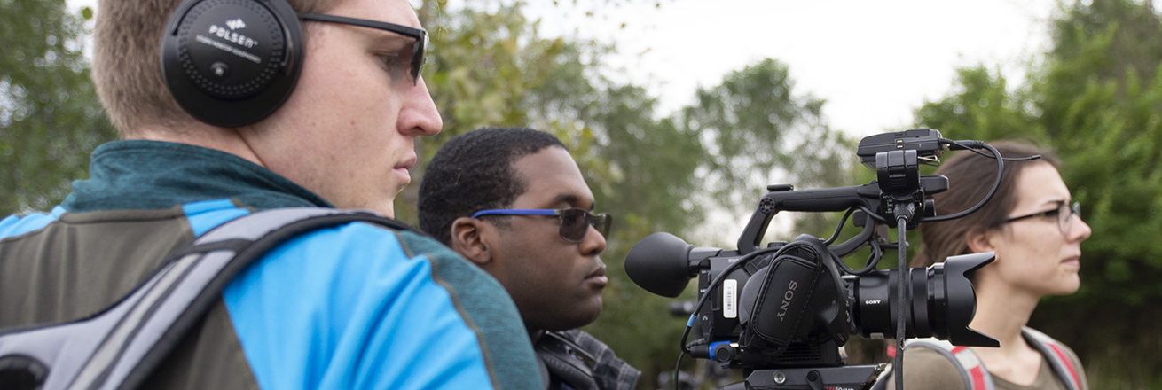 Three students standing with a film camera