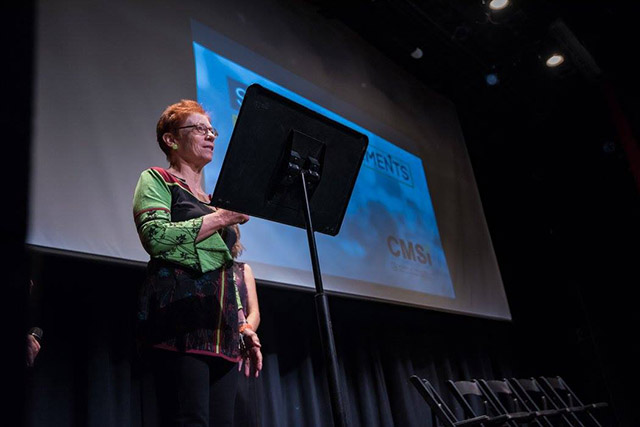 Professor Pat Aufderheide presenting in front of a powerpoint at Story Movements in the Greenberg Theater.