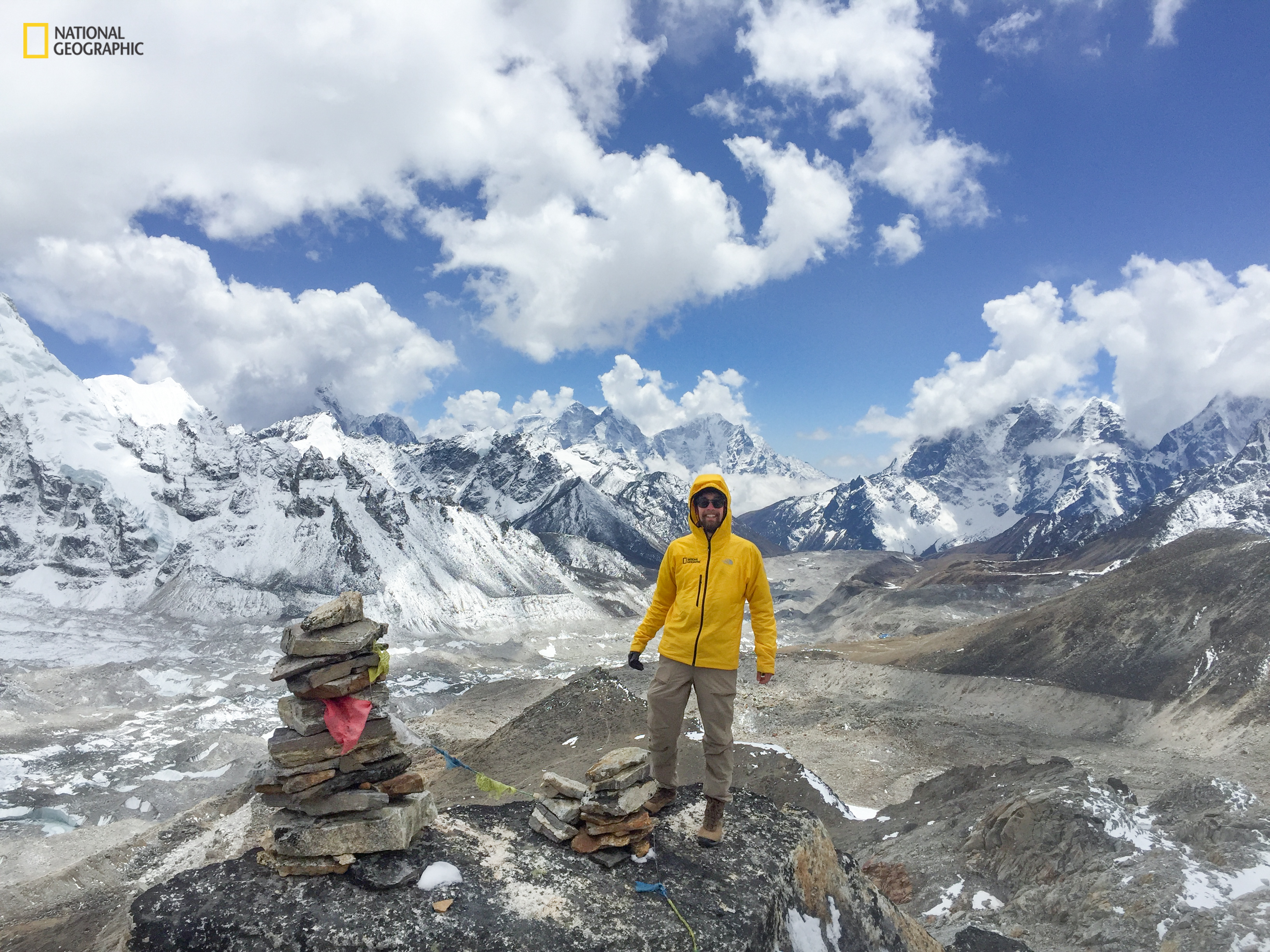 Sam Sheline in a rain coat standing in front of a large mountain