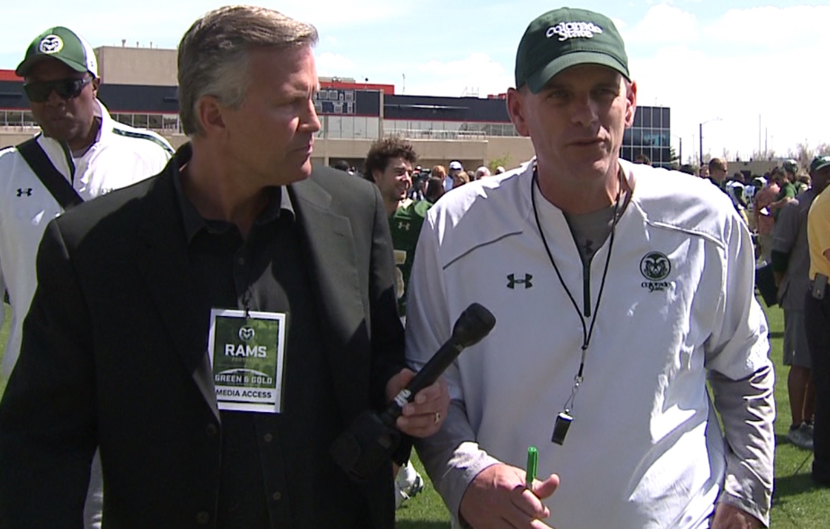 Reporter Chris Halsne interviewing a football coach on a field 
