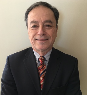 Andras Simonyi, an older man wearing a suit and tie stands before a beige background