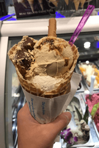 Big scoops of chocolate colored gelato in a cone with a purple spoon