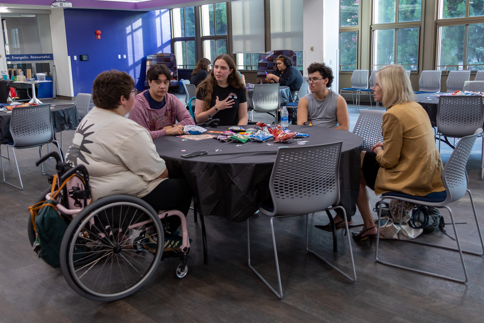 Students and a faculty member sit at a table at the Disability Connection Social. One student on the side of the table near the camera is in a wheelchair.