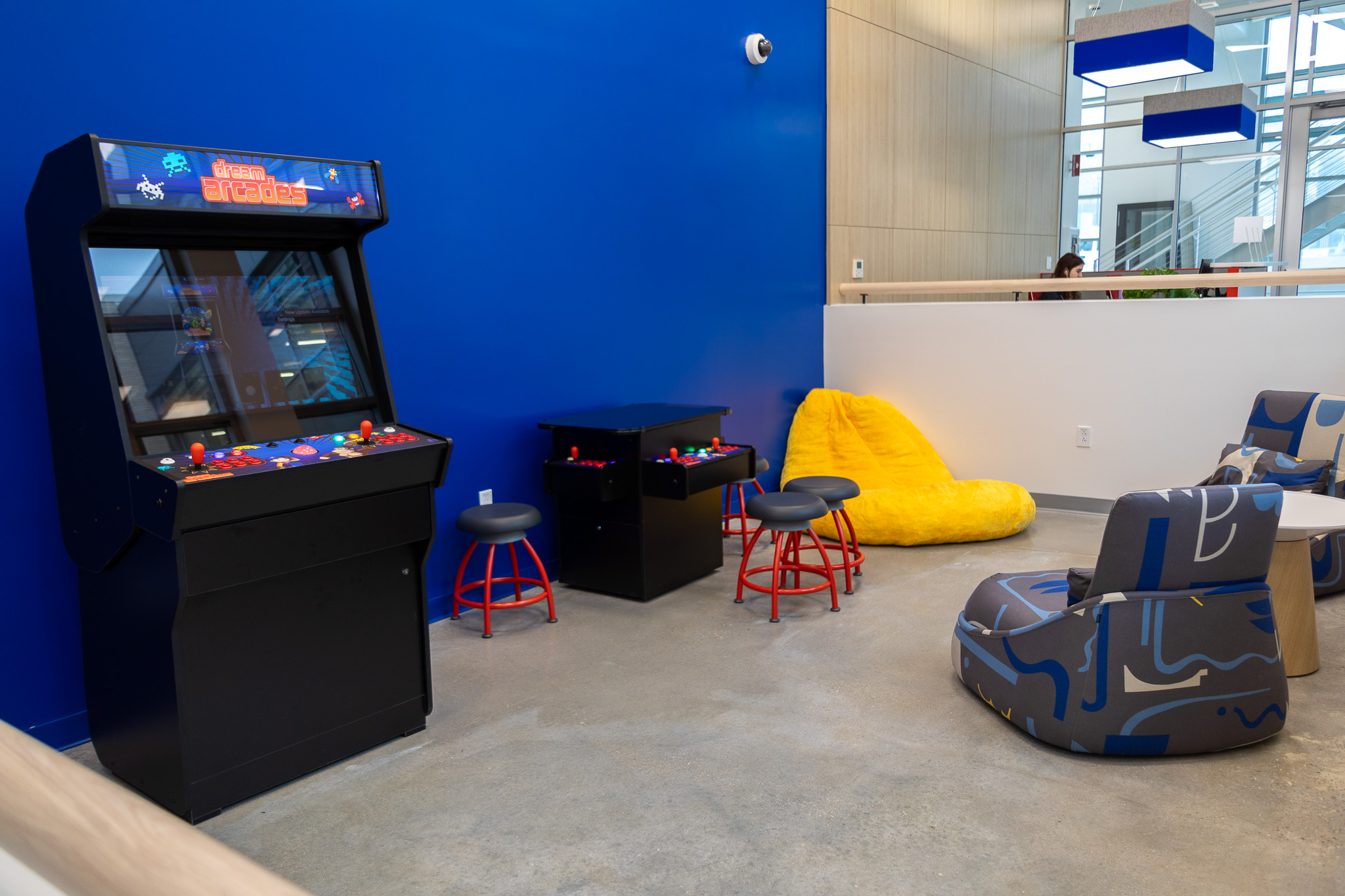 Two arcade machines sit against the wall.  Nearby, several bean bags and comfy chairs are on the floor.