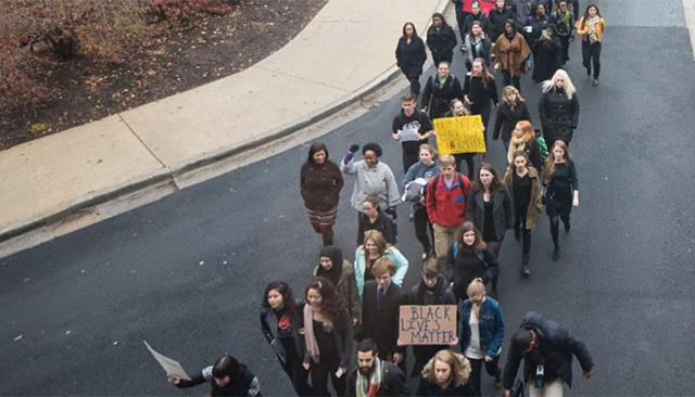A group of student protesters viewed from above. Several are holding signs, one reading "Black Lives Matter" is visible.