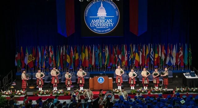 AU Commencement Setup Stage setup for commencement with flags along the back, podium in center, and people playing bag pipes lined across the front