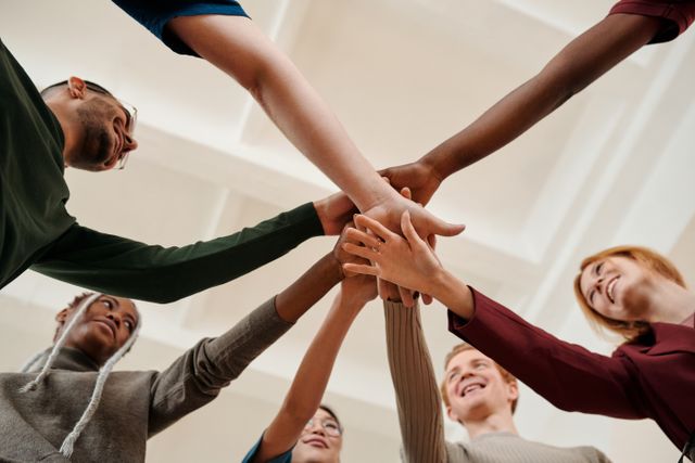 A diverse group of young adults forming a united circle with hands together indoors