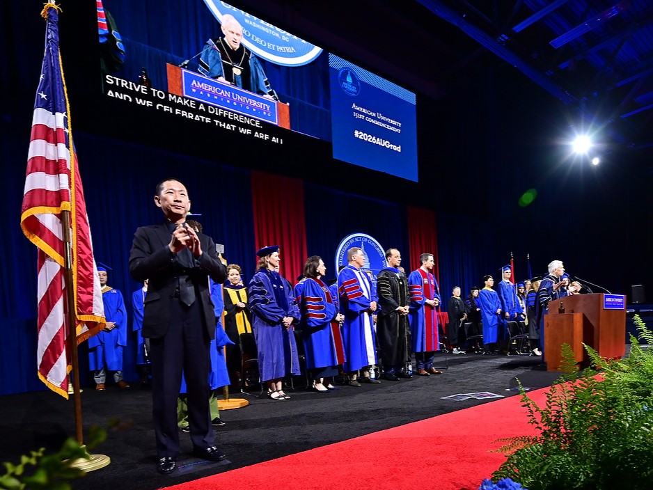 Sign language interpreter on commencement stage in front of a screen with closed captions