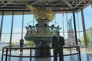 Professor Kraut stands in Statue of Liberty museum with windows behind him and torch too.
