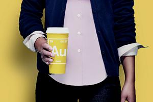 A photo of a young woman of color holding a coffee cup that has