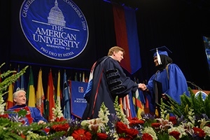 President Neil Kerwin shakes the hand of a new graduate as she crosses the stage.