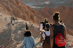 student wearing an AU backpack walks along a mountain trail abroad