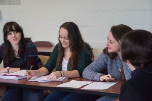 Students sitting around table in classroom taking notes.