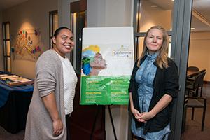 Amelia Tyson and Ashley Luke standing on either side of a sign at a conference.