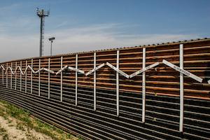 US Mexico border wall streching out beneath blue sky