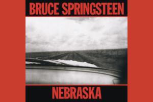 Cover art from Bruce Springsteen's album Nebraska; A car dashboard driving down a lonely road between empty fields; Black and white