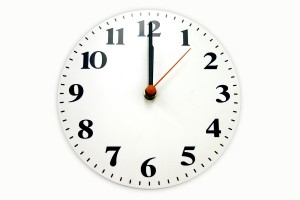 A white wall clock with the arms at twelve o clock