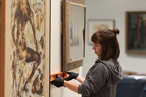 A person measures two art pieces on the wall at the AU museum.