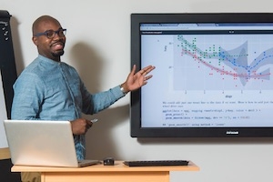 Data scientist standing in front of screen with data.