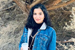 Eman Alghamdi standing in front of a tree holding a coffee cup