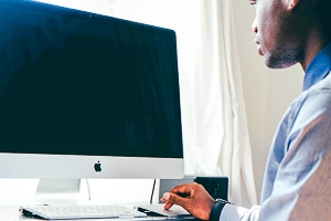 A young man in a blue button down stares at a mac.