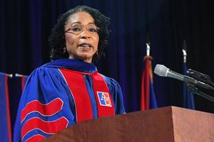 Woman with cap and gown at a podium while giving a speech.