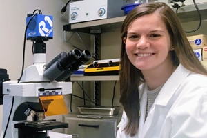 Grad student Linda Amarante seated next to a microscope.