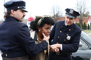 Two white police officers restrain a black woman.