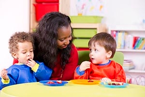 Children eating fruit at a nursery with their caretaker