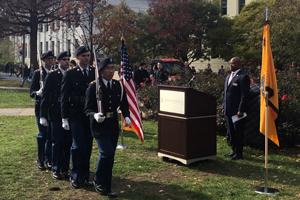 Soldiers carrying rifles, in front of American flag and podium